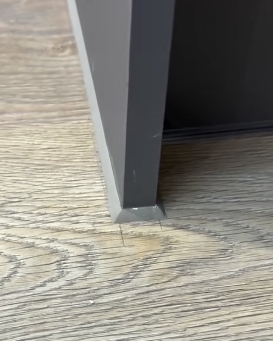 Grey silicone bead where a dark grey door frame meets wood-effect flooring
