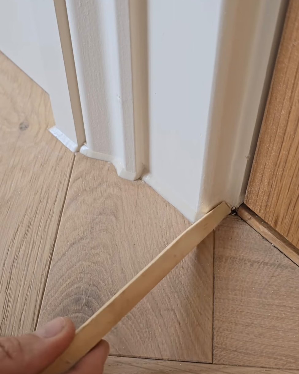 Silicone bead being tooled along skirting board above light oak flooring